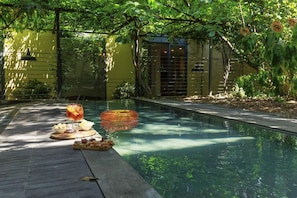 A poolside area with a dining setup including a drink and snacks, surrounded by greenery and a building with large windows.