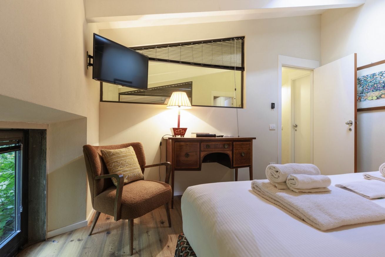 A hotel room with a bed, a desk, a chair, a TV mounted on the wall, and a window.
