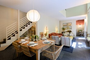 A dining area with a wooden table set for four, surrounded by wicker chairs. A staircase with a white railing leads to an upper level. - Duomo Luxury Apartment with plunge pool (Firenze)