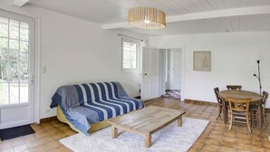 Ein großzügiger Wohnbereich mit einer Couch, einem Holztisch, einem Esstisch mit Stühlen und einer Pendelleuchte.