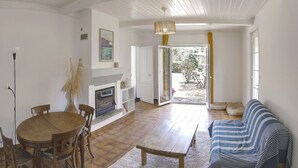 Ein Wohnzimmer mit einem Holzesstisch, Stühlen, einer Couch, einem Kamin und Blick durch eine Glastür.