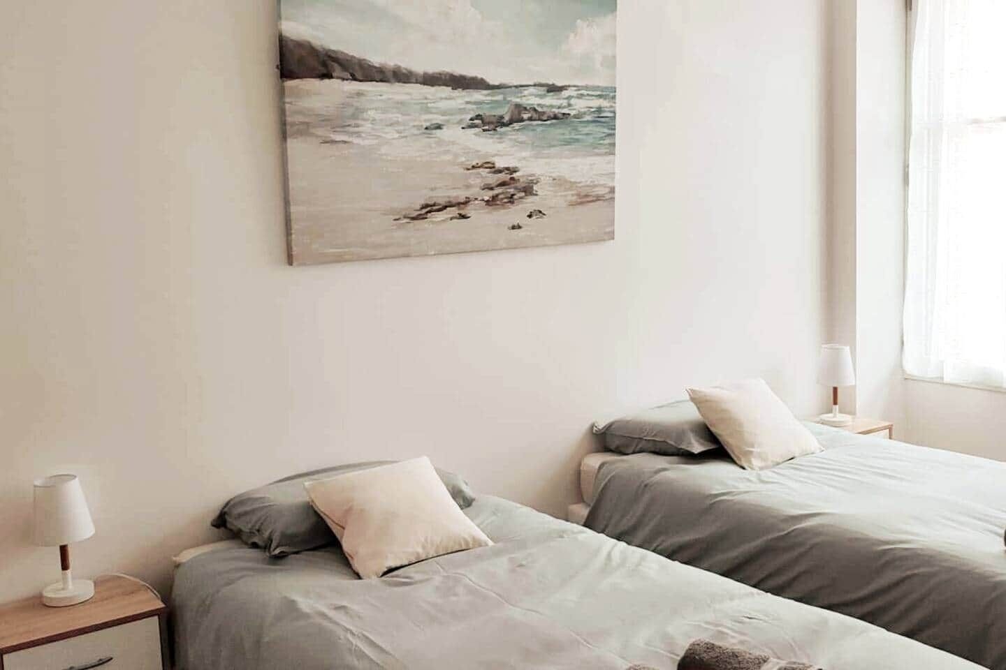 Una camera da letto con due letti, un quadro che raffigura una spiaggia e una finestra con tende.
