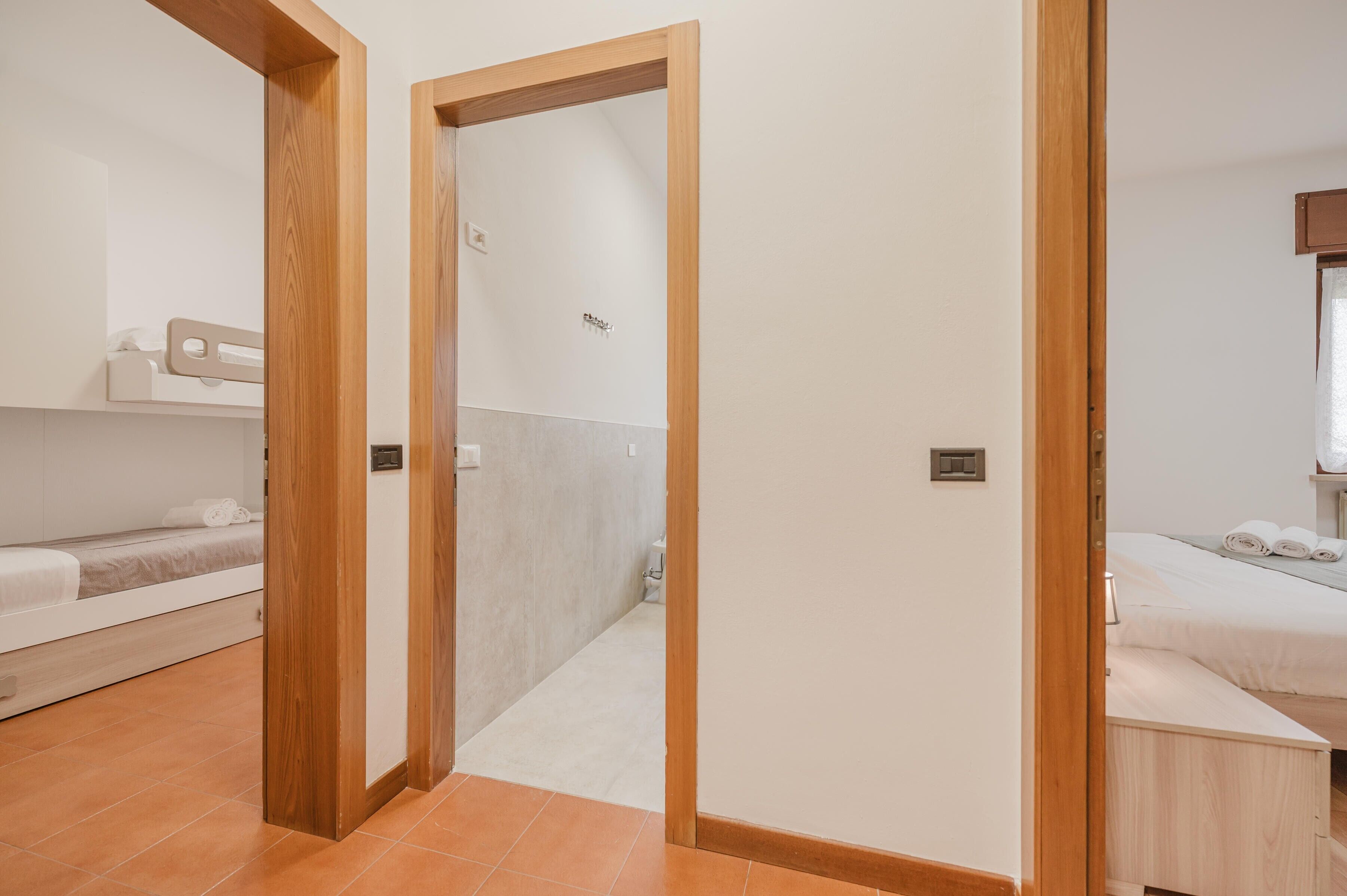 Una habitación de hotel con una puerta de madera, una cama con sábanas blancas, una mesita de noche pequeña y un interruptor de luz en la pared.