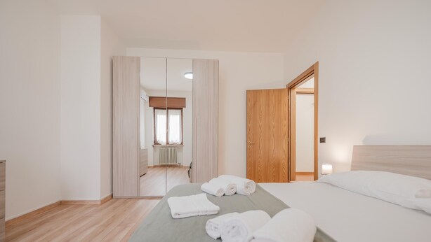 Ein Hotelzimmer mit Bett, Holzschrank, Spiegel und Blick auf einen Flur.