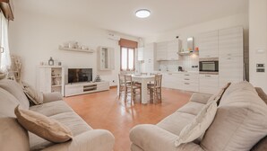 Ein modernes Wohnzimmer mit einer Couch, einem Esstisch und einer Küchenzeile mit Schränken und Geräten.