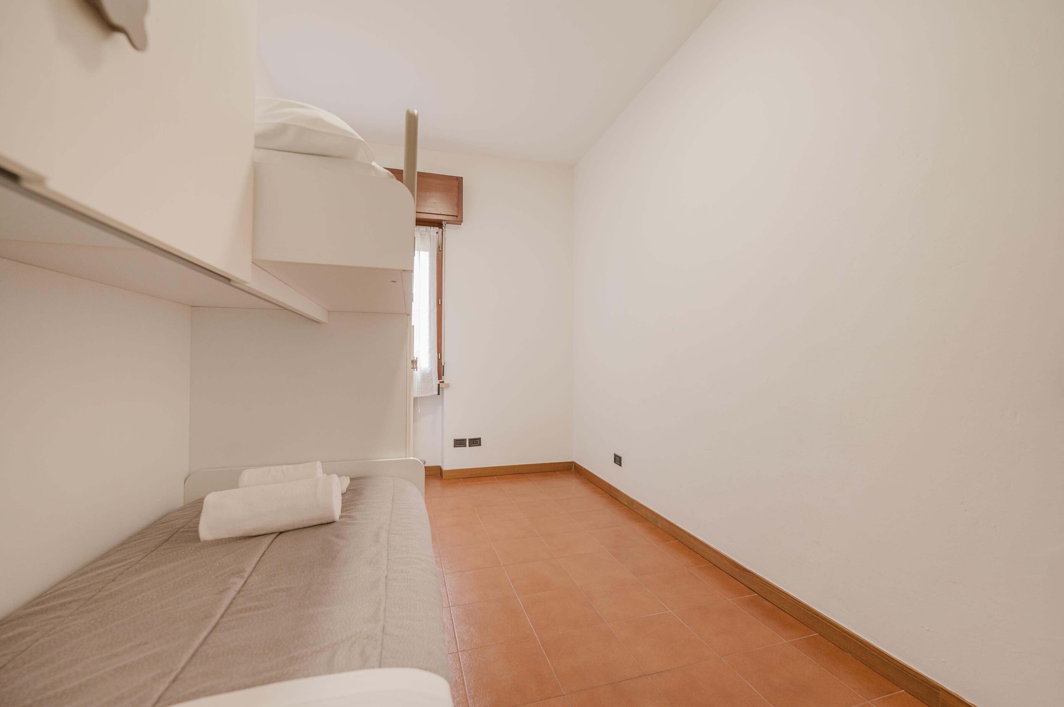 A small, clean room with a bunk bed, a bedside table, and a door leading to another room.