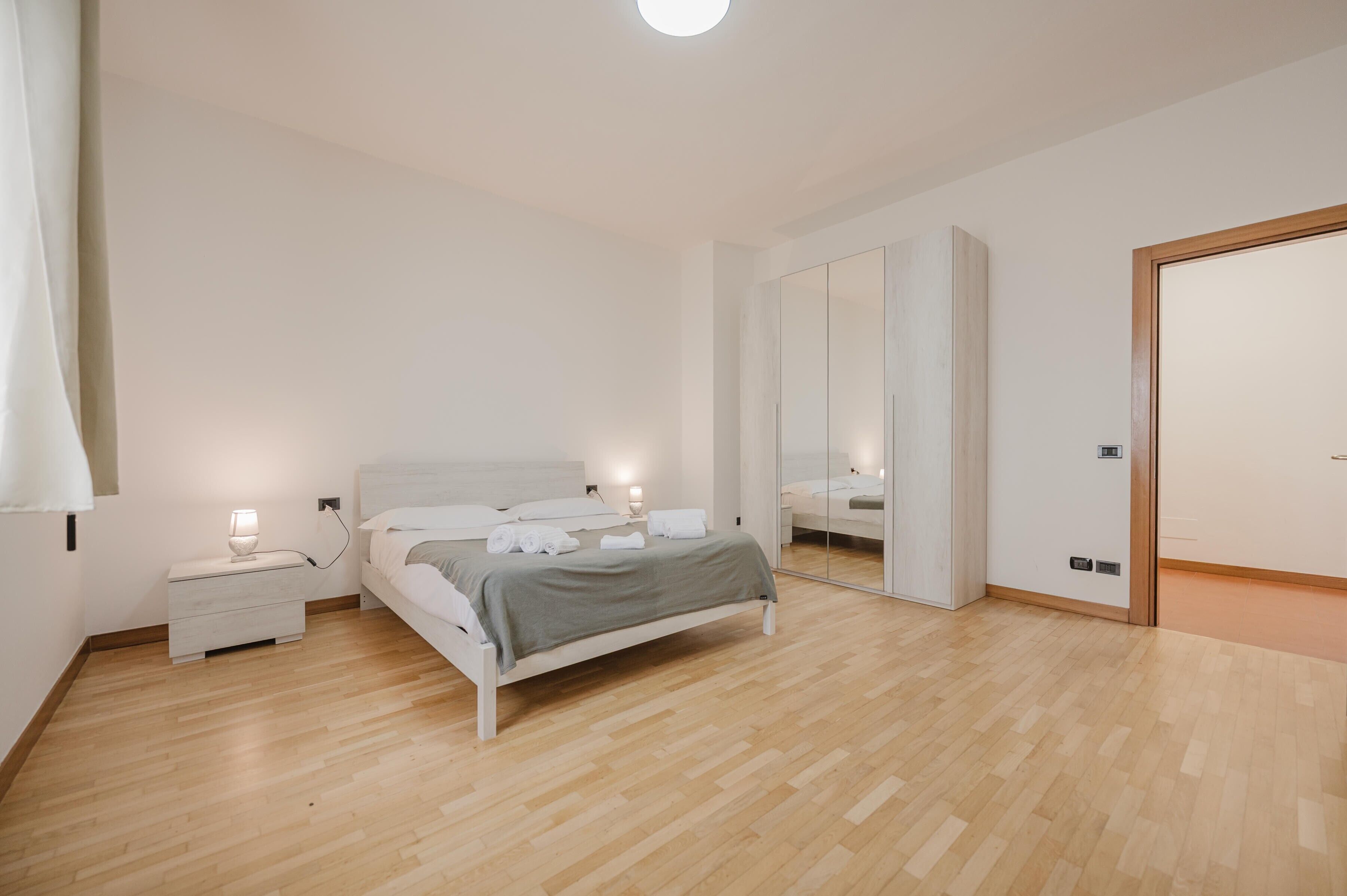 Ein Schlafzimmer mit einem Bett, Nachttischen, einem Spiegel und einem Kleiderschrank.