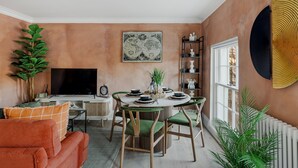 A cozy living room with a round table, green chairs, a television, and a large globe artwork on the wall. - 2 Bedroom Apartment-Kings Cross (London)