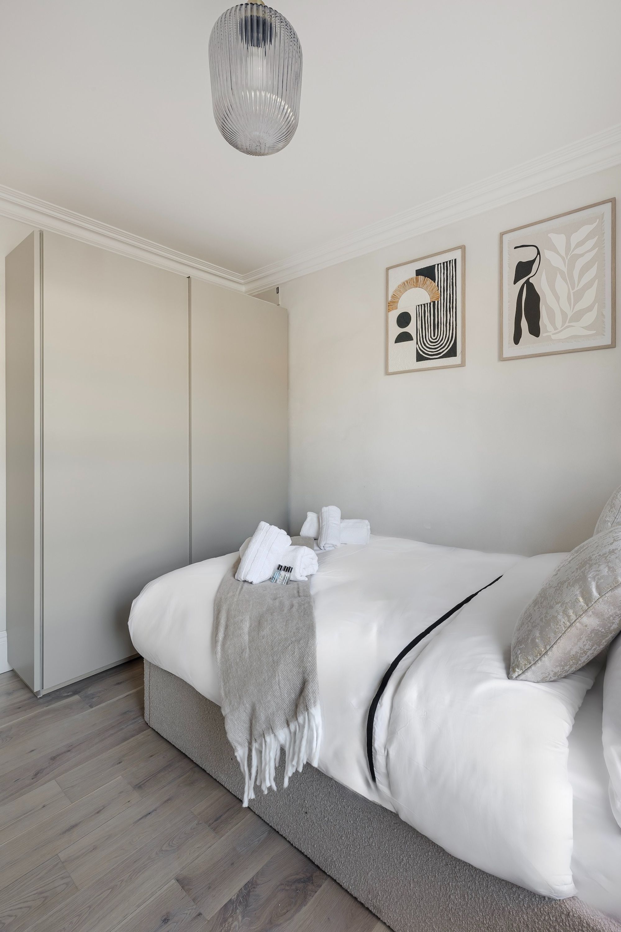 Ein ordentlich eingerichtetes Schlafzimmer mit einem Bett, einem Kleiderschrank und zwei gerahmten Kunstwerken an der Wand.