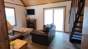 A cozy living room with a wooden ceiling, a ceiling fan, a fireplace, a sofa, a coffee table, and a staircase. - Cozy Lakefront 2-bedroom cabin in tranquil Big Sandy, TX. (Big Sandy)