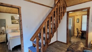 A spacious living area with a wooden staircase, a brown leather sofa, and a bed in the background. - Cozy Lakefront 2-bedroom cabin in tranquil Big Sandy, TX. (Big Sandy)