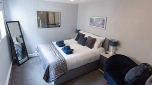 Quarto de hotel com cama, mesa de cabeceira, cadeira, espelho e um quadro na parede.