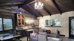 A cozy living room with a dining area, a kitchen with wooden cabinets, and a large window.