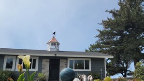A house with a stone facade, a small tower-like structure on the roof, and a garden with succulents and a large decorative sphere.