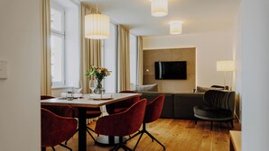 A modern living room with a wooden dining table, red chairs, a grey sofa, and a flat-screen TV mounted on the wall.