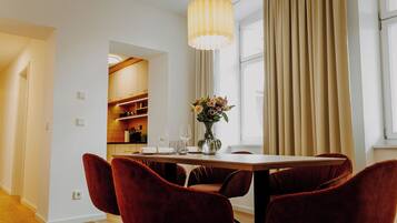 A dining area with a wooden table, red velvet chairs, a vase with flowers, and a large window with curtains.