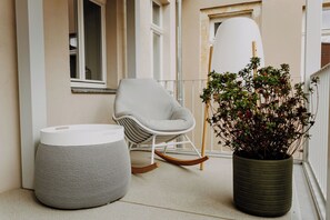 Un balcón con una mecedora blanca, un reposapiés tejido y una planta en maceta.