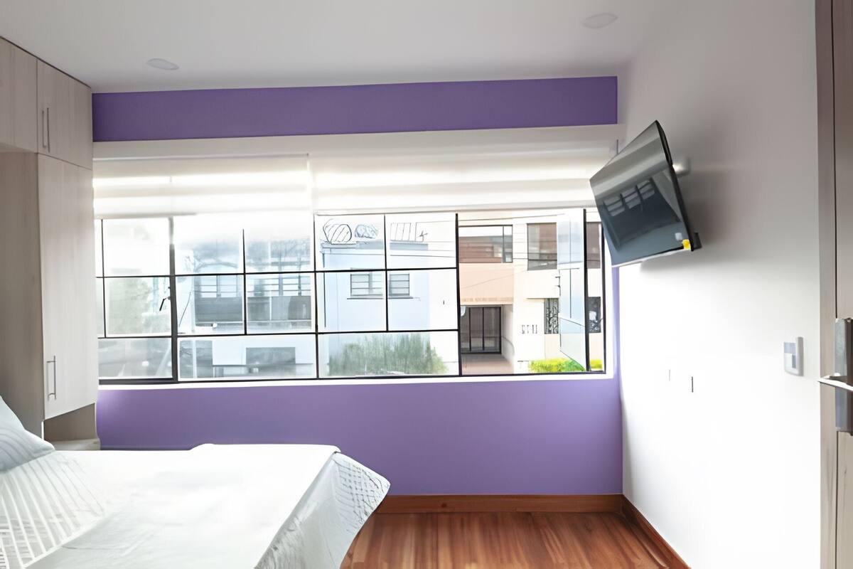 A bedroom with a large window, a bed, and a mounted TV.