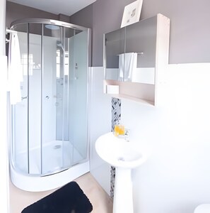 Ein modernes Badezimmer mit Duschkabine aus Glas, einem weißen Waschbecken und einem Spiegel darüber.