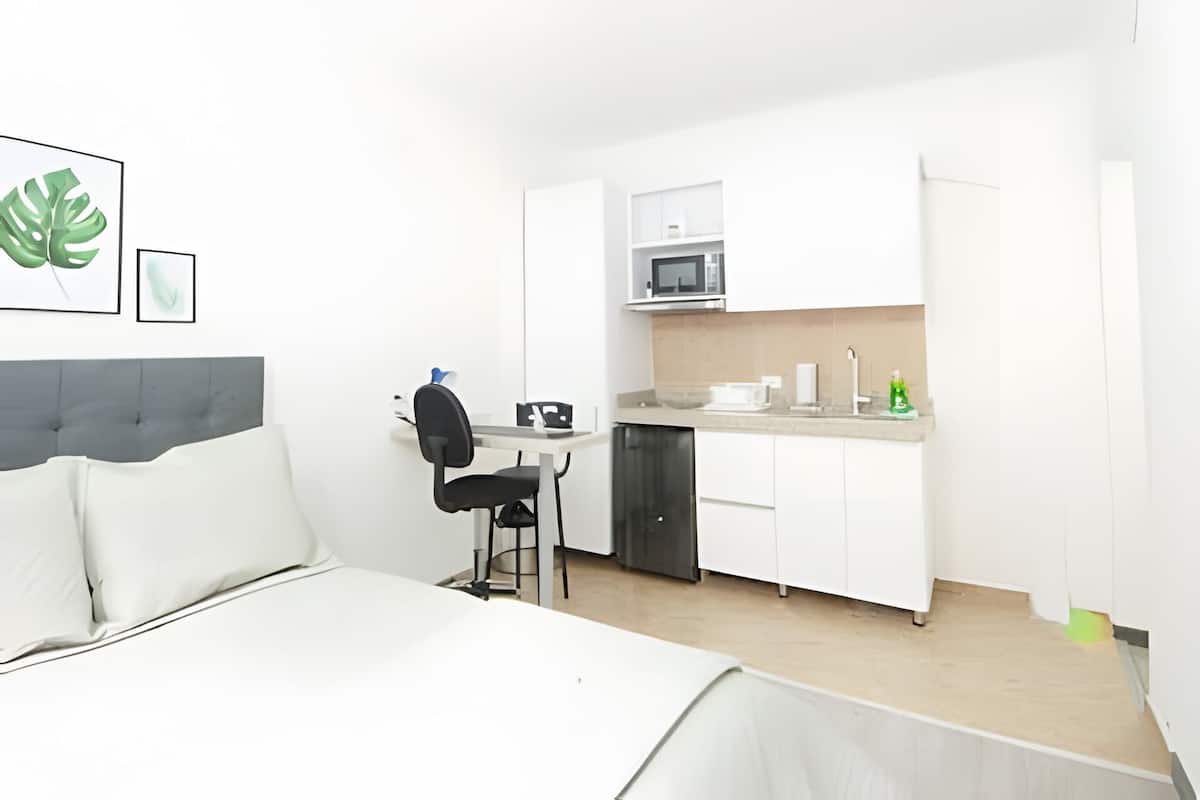 A small, modern room with a bed, a desk, and a kitchenette.