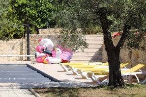 A poolside area with lounge chairs, a stone wall, and a tree.