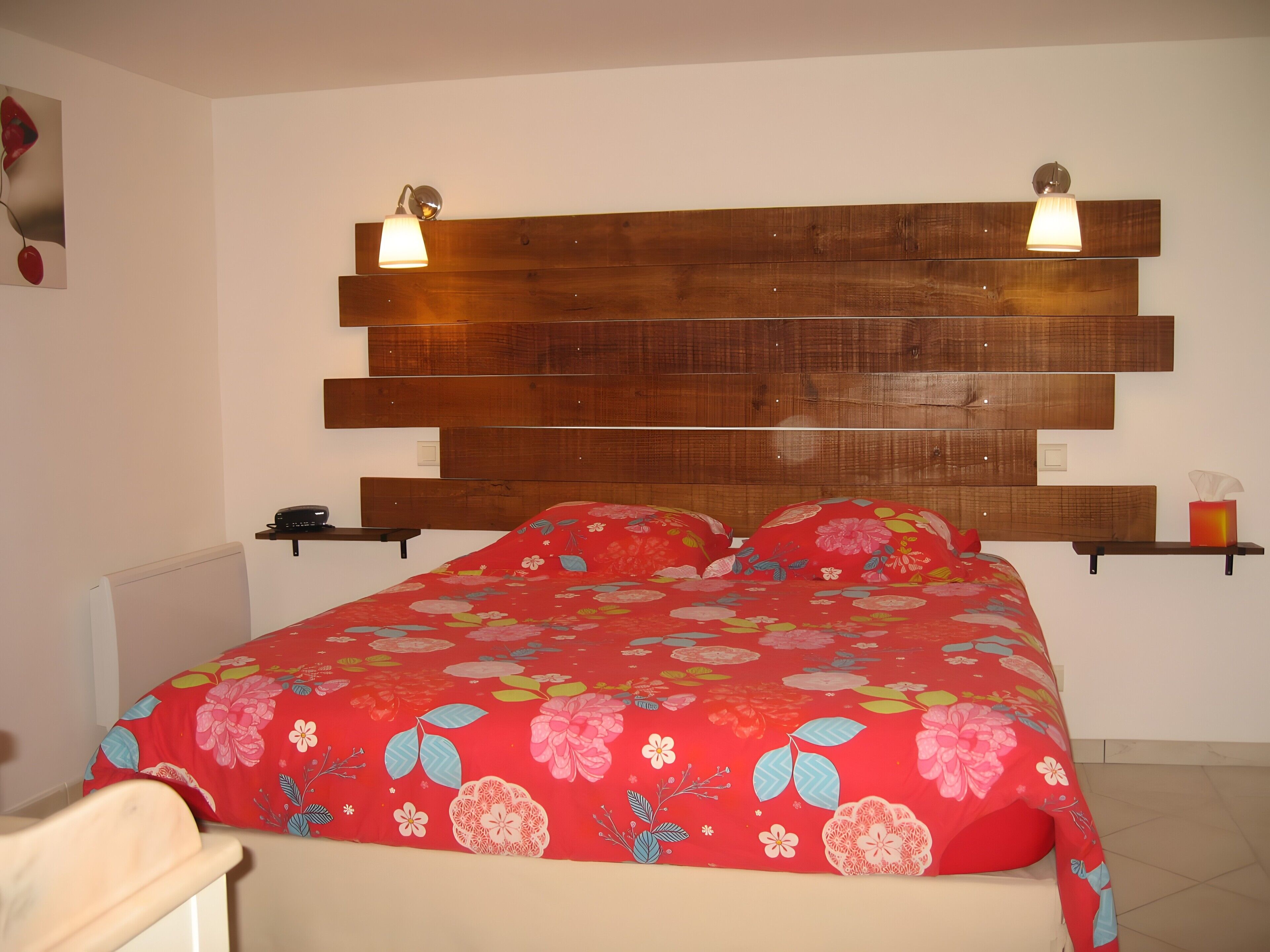 Ein Schlafzimmer mit einem Holzkopfteil, einer floralen Bettdecke, Nachttischen und einer Wandlampe.