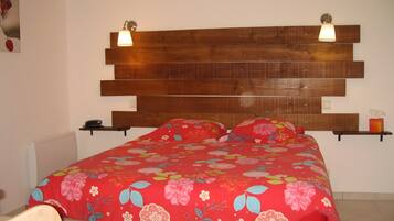 Ein Schlafzimmer mit einem Holzkopfteil, einer floralen Bettdecke, Nachttischen und einer Wandlampe.