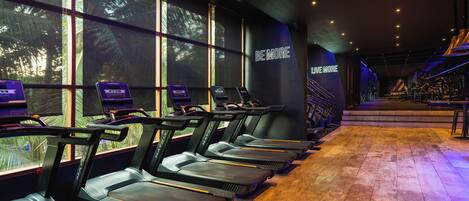 Varias cintas de correr en un gimnasio, con un cartel en la pared que dice 'BE MORE LIVE MORE'.