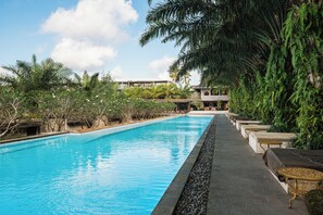 A swimming pool with a stone edge, surrounded by lush greenery and palm trees. - ONYX Park Resort Ubud (Ubud)