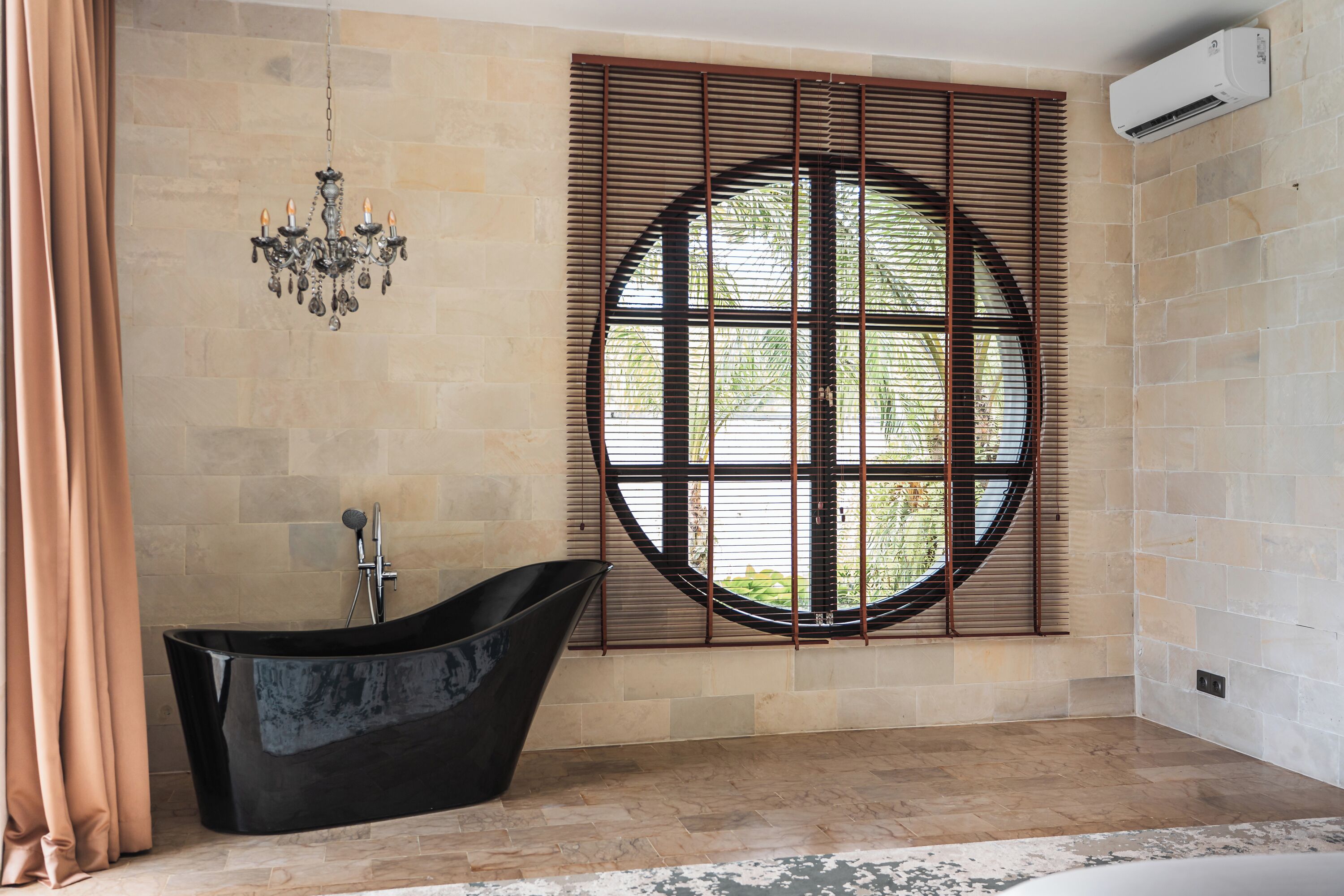 A modern bathroom with a freestanding bathtub, a large window with blinds, and a wall-mounted air conditioner.