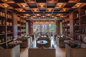 A spacious interior with multiple seating areas, wooden shelves with decorative items, and large windows offering views of the outside. - ONYX Park Resort Ubud (Ubud)