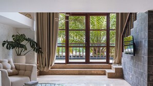 Un salón amplio con un ventanal grande, un sofá color beige, una mesita de centro de vidrio y una planta en maceta.