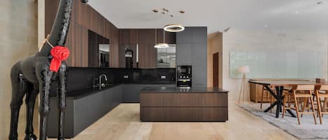 A modern kitchen with dark cabinetry, a central island, and a dining area with a table and chairs.