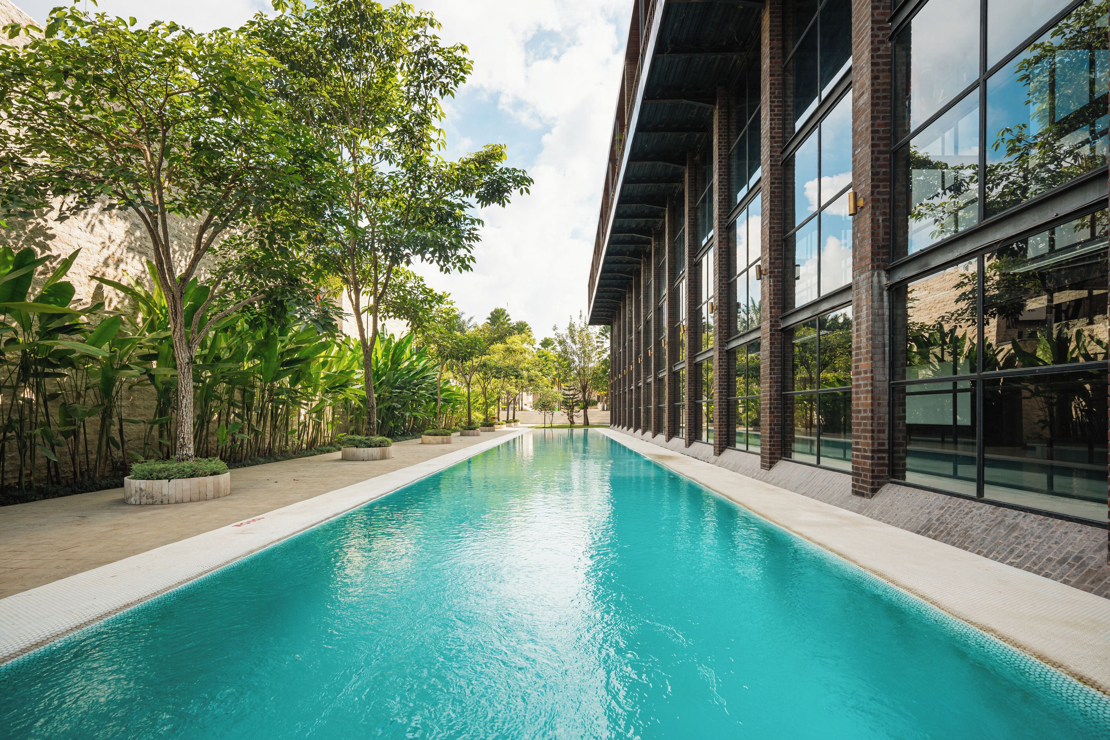 A swimming pool with a clear blue water surface, surrounded by lush greenery and modern architecture.