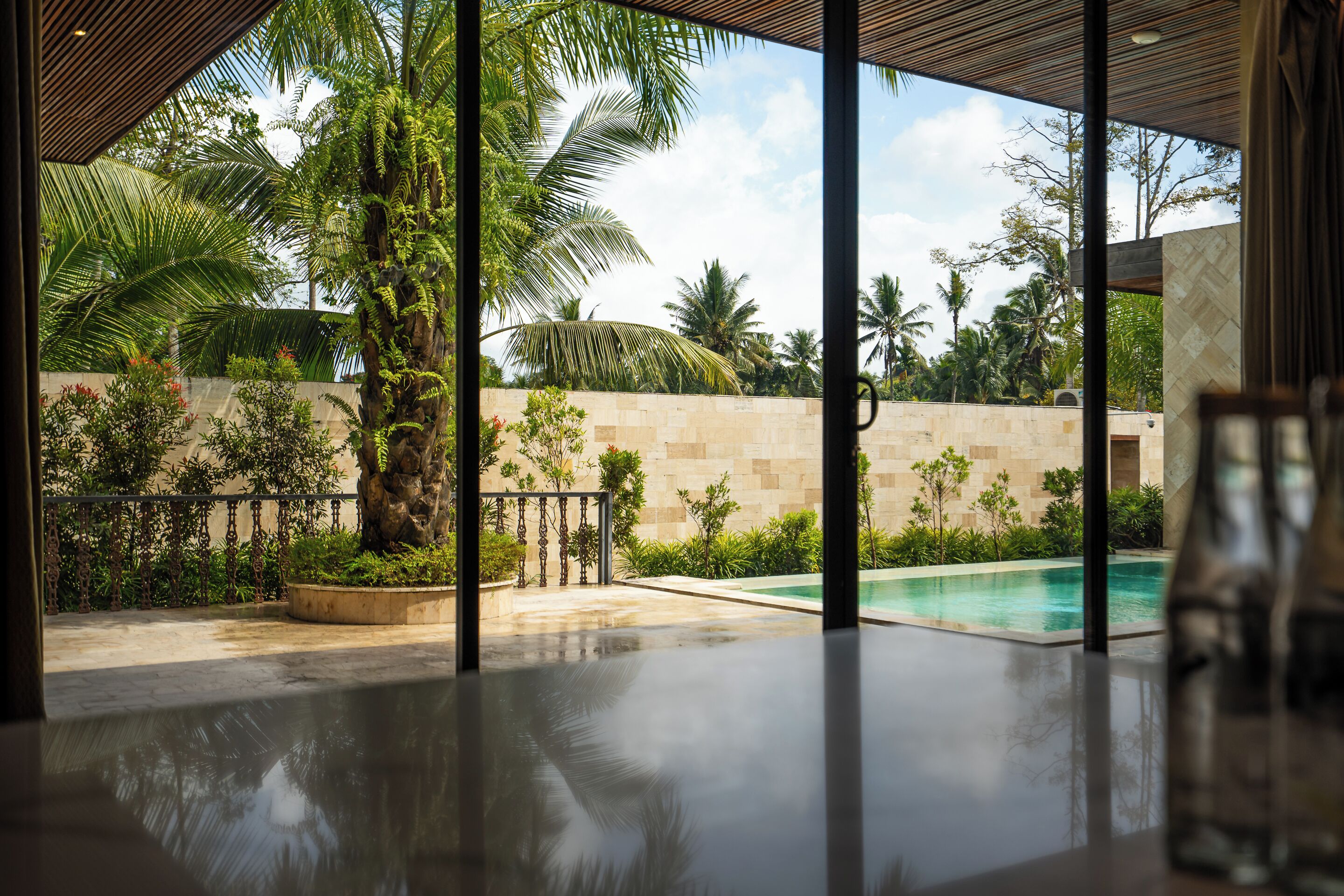 A modern poolside area with a clear view of a swimming pool, surrounded by lush greenery and a stone wall.