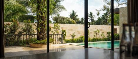 A modern poolside area with a clear view of a swimming pool, surrounded by lush greenery and a stone wall.