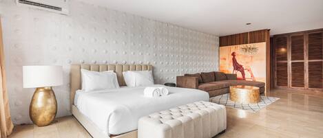 A modern hotel room with a large bed, a sofa, a round coffee table, and a decorative wall.