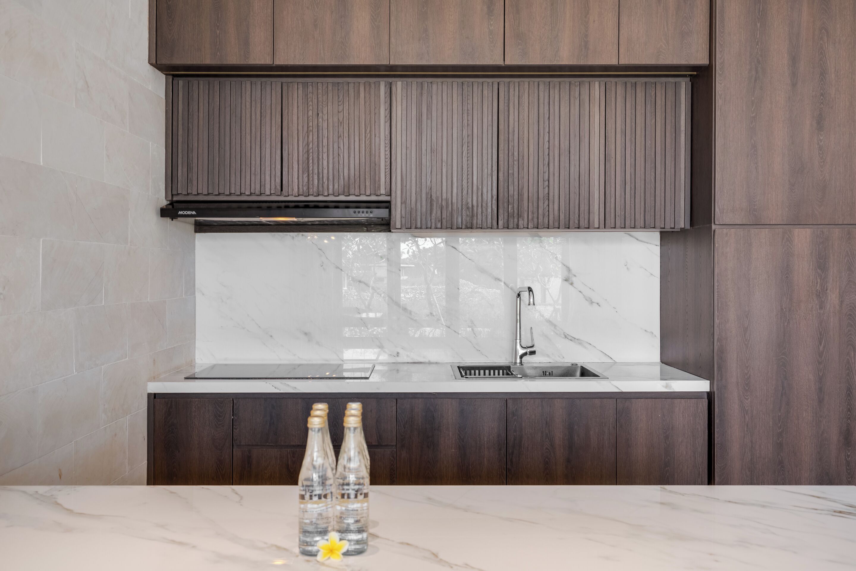 A modern kitchen with dark wood cabinets, a marble countertop, and a stainless steel sink.
