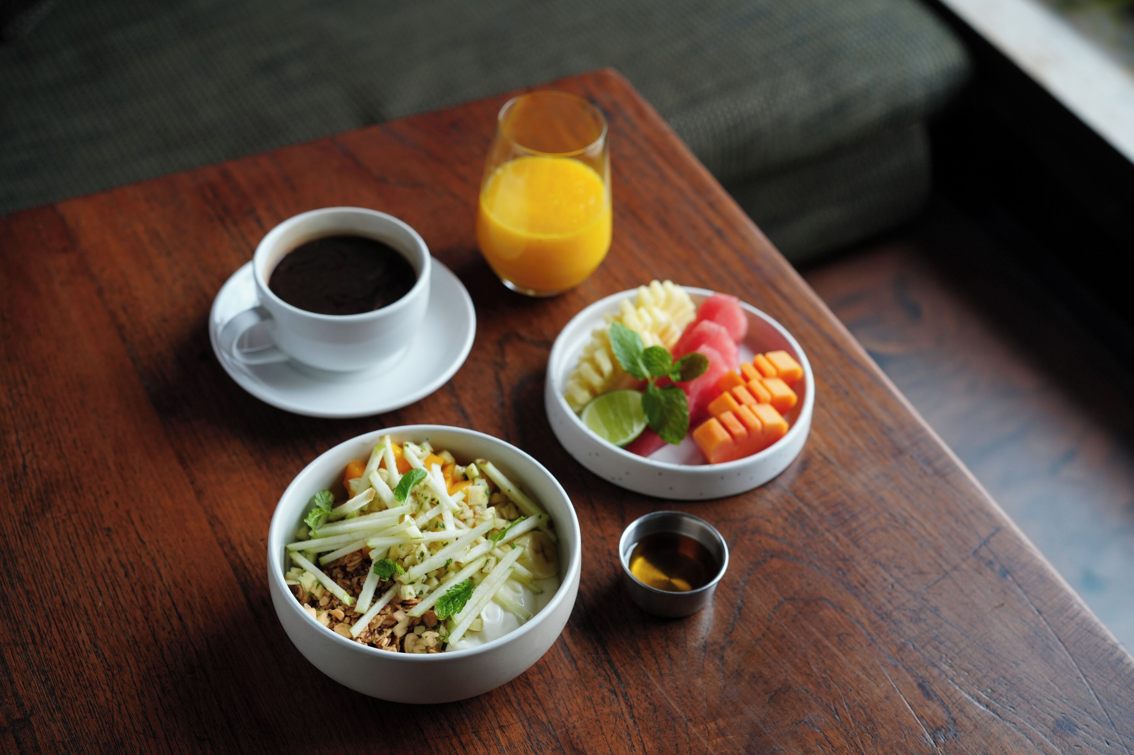 A wooden table with a white cup of coffee, a glass of orange juice, and two bowls of food.