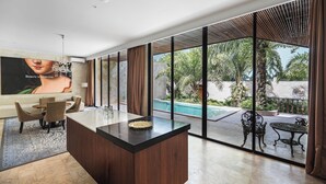 A modern living room with a large glass door leading to a pool area, a wooden dining set, and a large TV screen displaying an image. - ONYX Park Resort Ubud (Ubud)