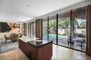 A modern living room with a large glass door leading to a pool area, a wooden dining set, and a large TV screen displaying an image. - ONYX Park Resort Ubud (Ubud)