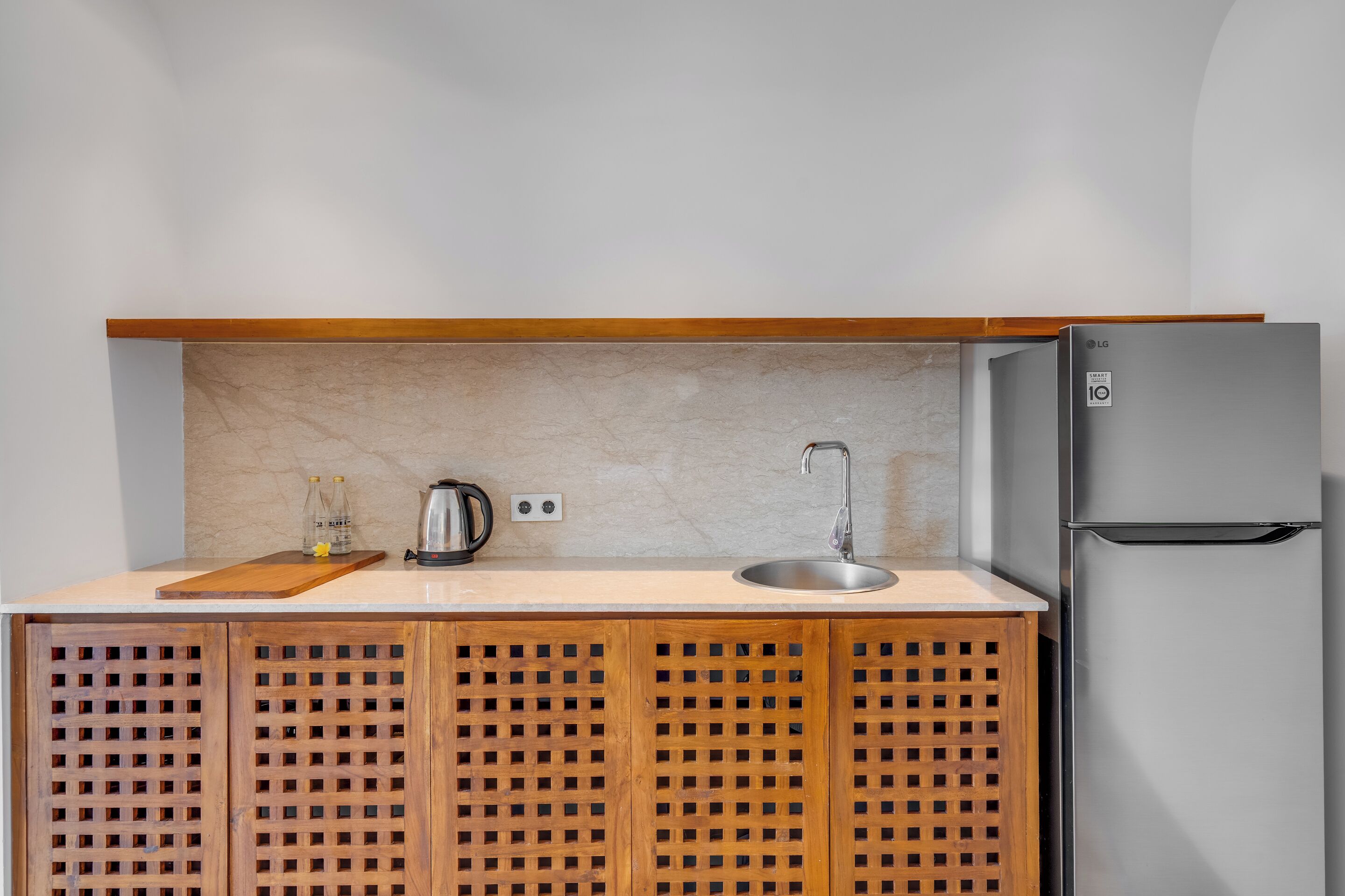 A compact kitchen with a built-in refrigerator, a wooden cabinet with a lattice design, a countertop, a sink, and a kettle.