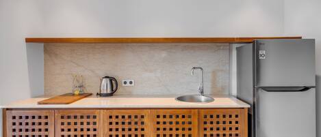 A compact kitchen with a built-in refrigerator, a wooden cabinet with a lattice design, a countertop, a sink, and a kettle.
