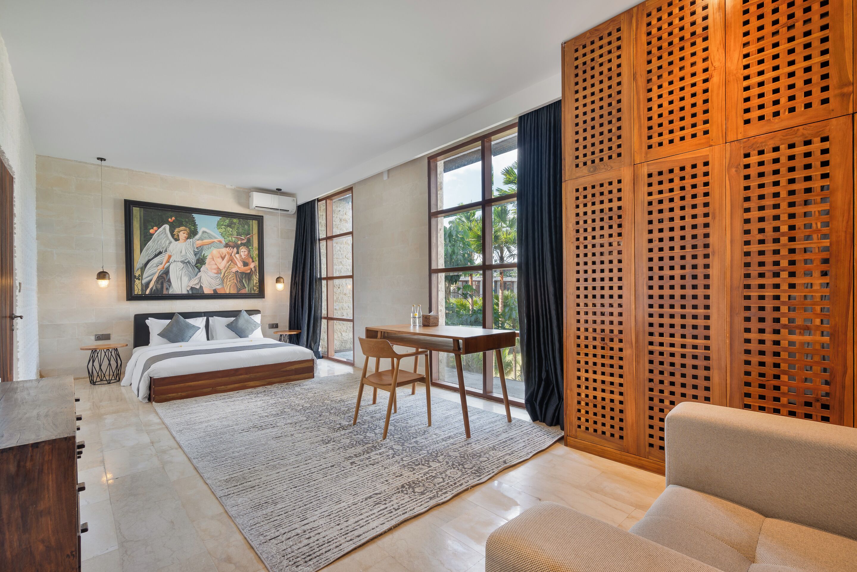 A bedroom with a bed, a desk, a chair, a sofa, a large window, and a wooden partition.