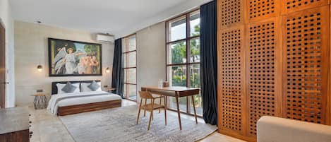 A bedroom with a bed, a desk, a chair, a sofa, a large window, and a wooden partition.