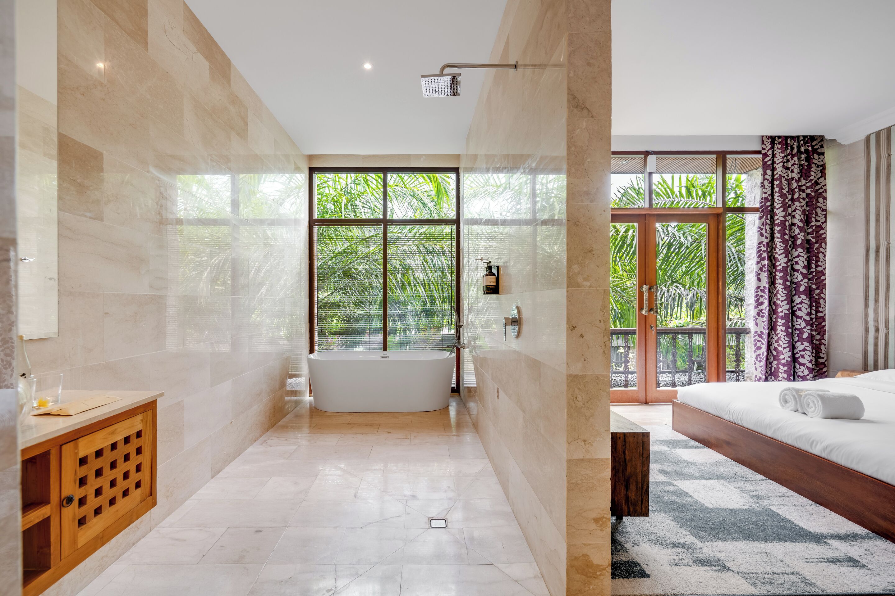A modern bathroom with a freestanding bathtub, a showerhead, and a large window with a view of greenery.