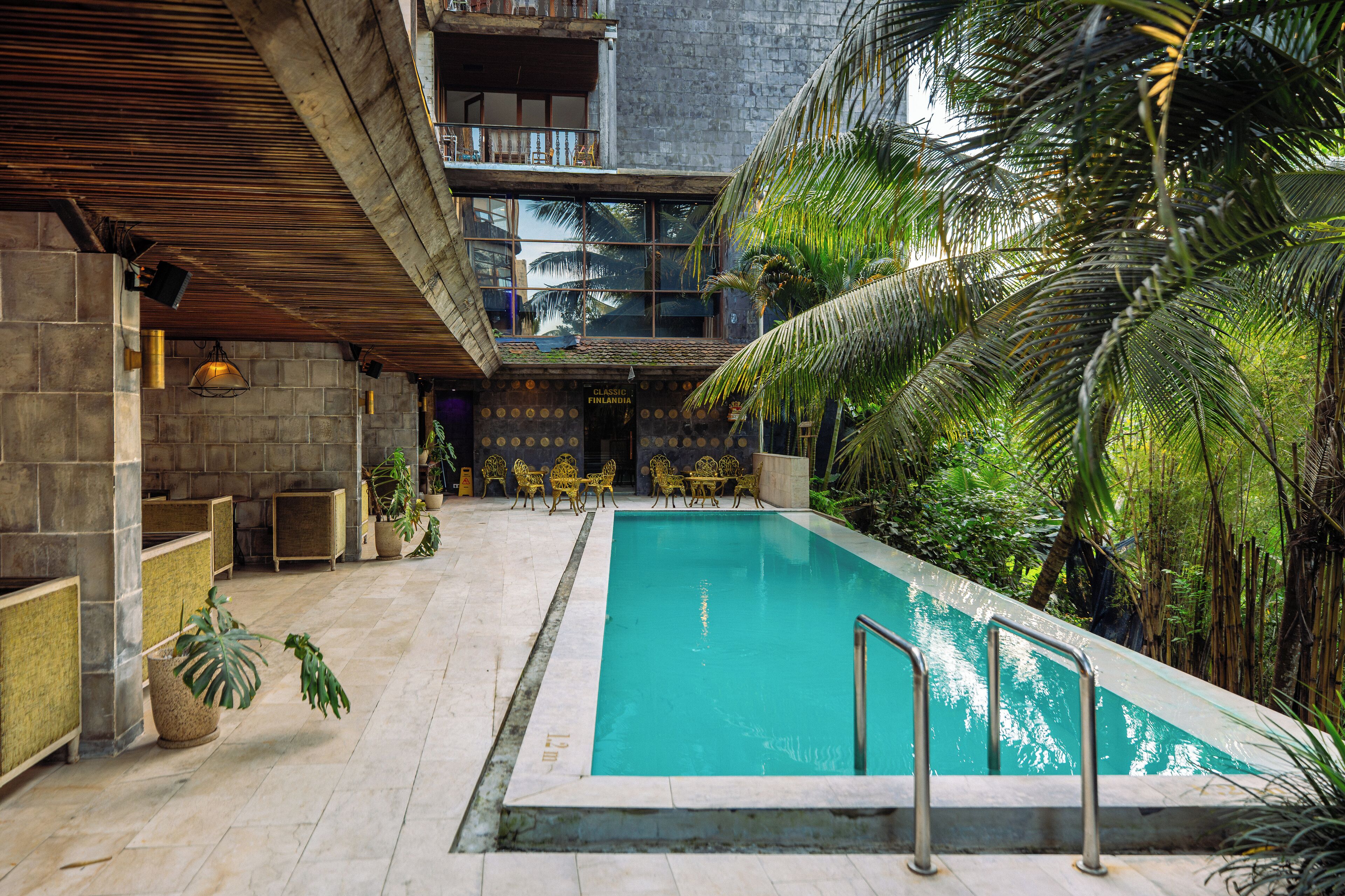 A pool area with a stone floor, surrounded by potted plants and a seating area with chairs and tables.