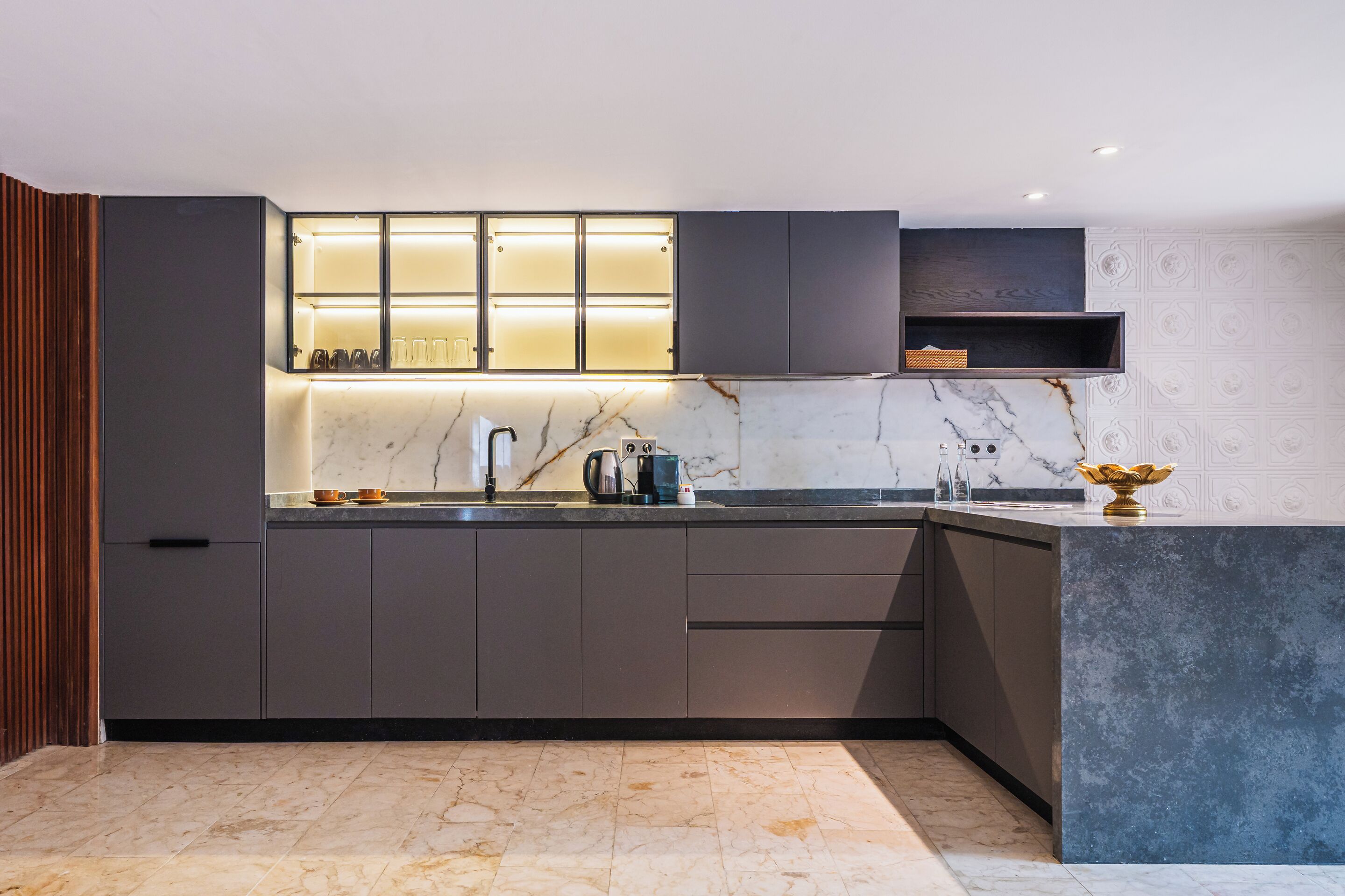 A modern kitchen with dark cabinetry, a marble countertop, and under-cabinet lighting.