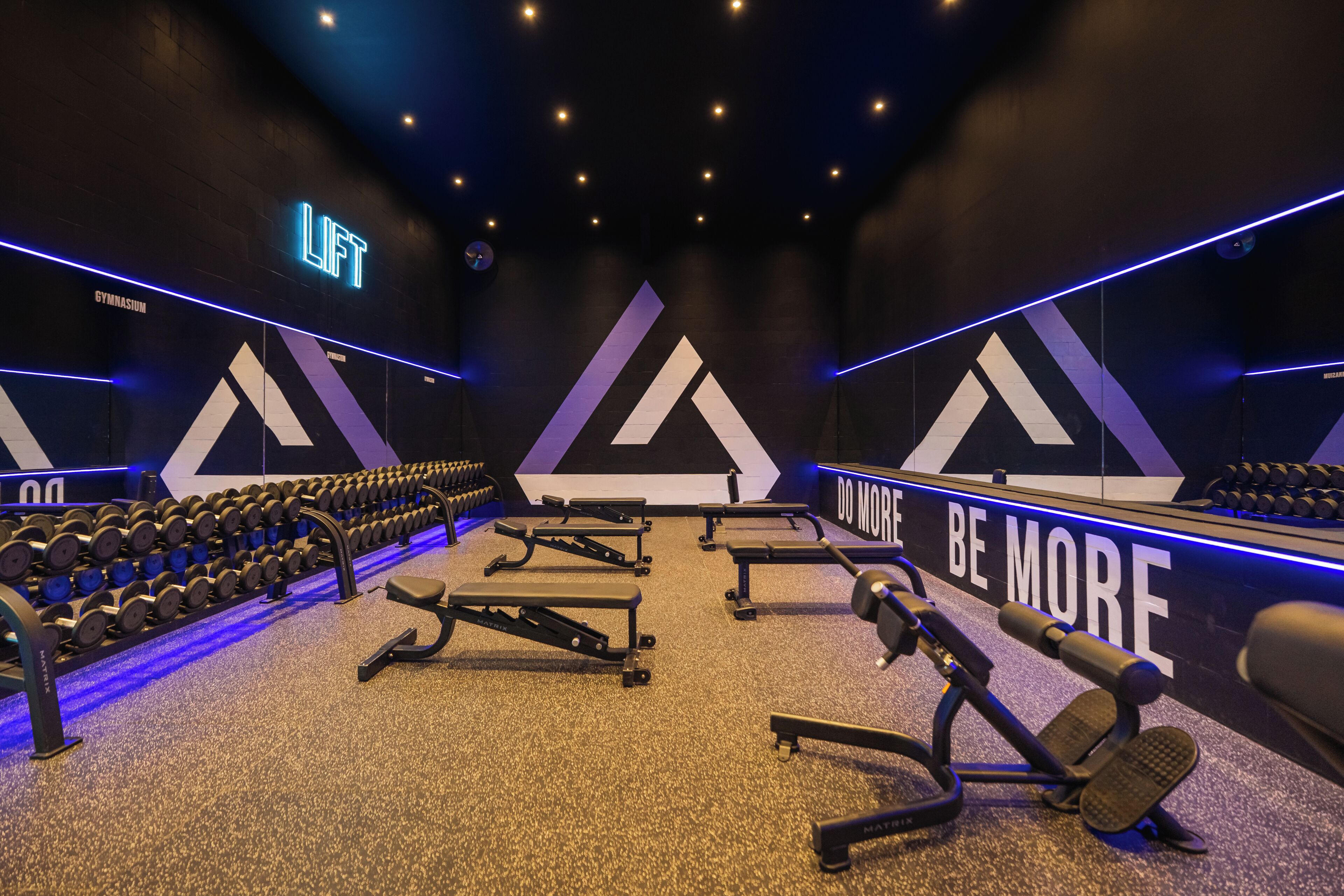 A gym with weightlifting equipment, dumbbells, and motivational wall text.