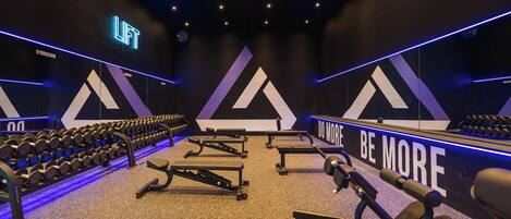 A gym with weightlifting equipment, dumbbells, and motivational wall text.
